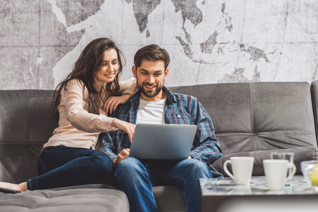 Look at this. Happy loving couple is using laptop at home. Girl is pointing finger at screen and smiling